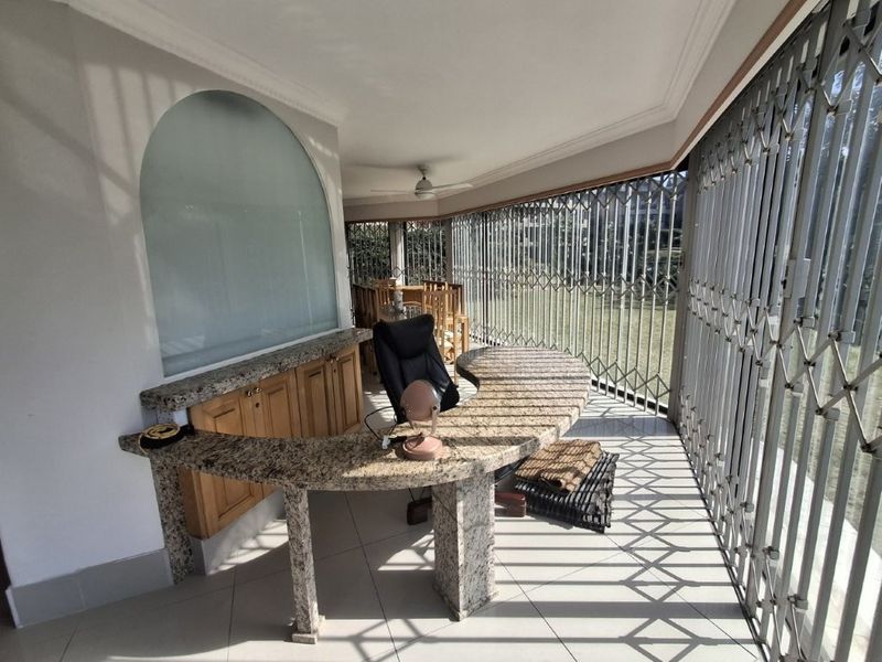 Enclosed patio area featuring a built-in granite desk or bar counter, tiled flooring, ceiling fan, and secure metal security gates overlooking the garden.