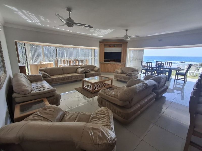 Spacious open-plan living and dining area featuring large porcelain tiles, ceiling fans, and expansive sliding doors with direct ocean views.