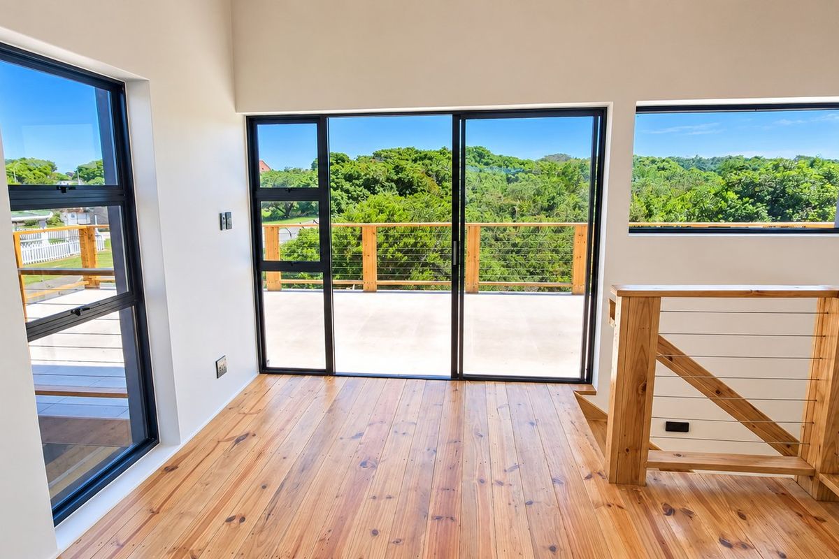 Bright and airy living space featuring polished timber flooring, modern aluminium-framed windows, and direct access to an outdoor balcony with scenic views.