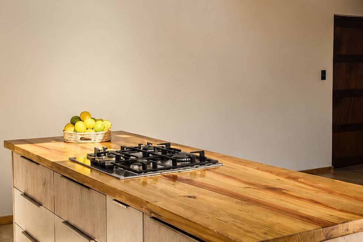 Modern kitchen island featuring a natural timber countertop, integrated gas hob, and stylish pendant lighting, set within an open-plan space with timber staircase.