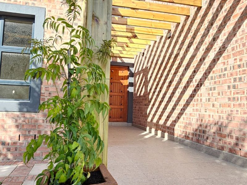 A well-maintained outdoor patio area featuring a timber pergola, brick wall construction, and a solid timber entrance door.
