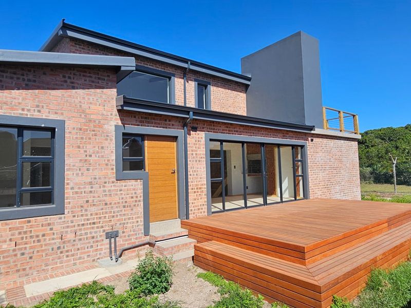 Rear view of a modern brick house featuring a spacious timber deck, large sliding glass doors, and a prominent chimney stack.