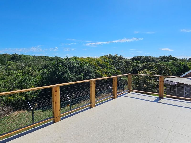 An elevated balcony featuring a modern timber and wire cable balustrade with tiled flooring, offering expansive views of the surrounding natural landscape.