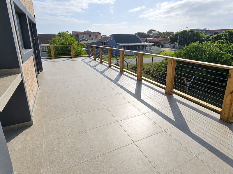 Spacious outdoor balcony featuring modern tiled flooring, a timber balustrade with cable railing, and a built-in concrete counter area.