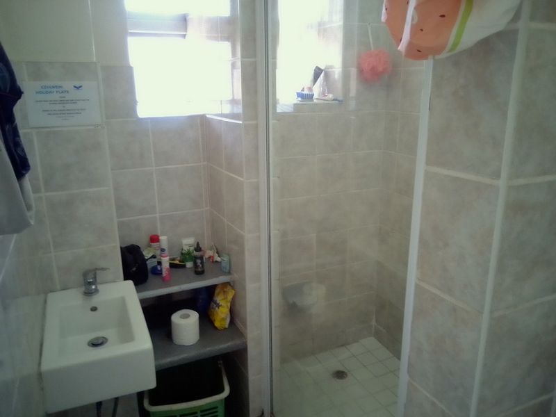 A compact bathroom featuring a wall-mounted basin, tiled finishes, and a glass-enclosed shower stall.