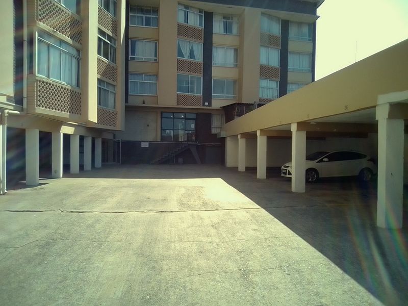 Exterior view of an apartment building featuring a concrete driveway and covered parking bays.