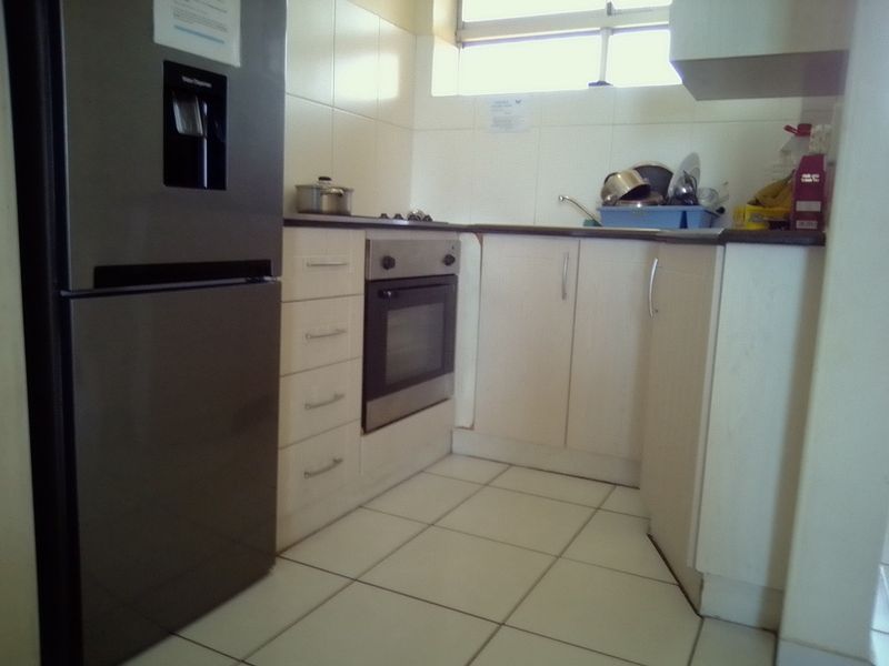 A compact kitchen featuring built-in cabinetry, a fitted oven and hob, tiled flooring, and a tiled backsplash.
