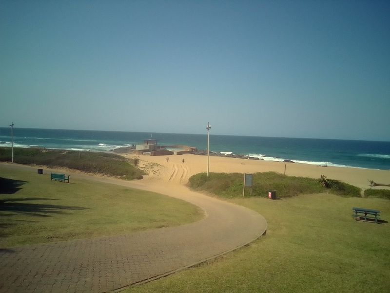 A scenic view of the coastal landscape featuring a paved walkway leading towards the beach and ocean.