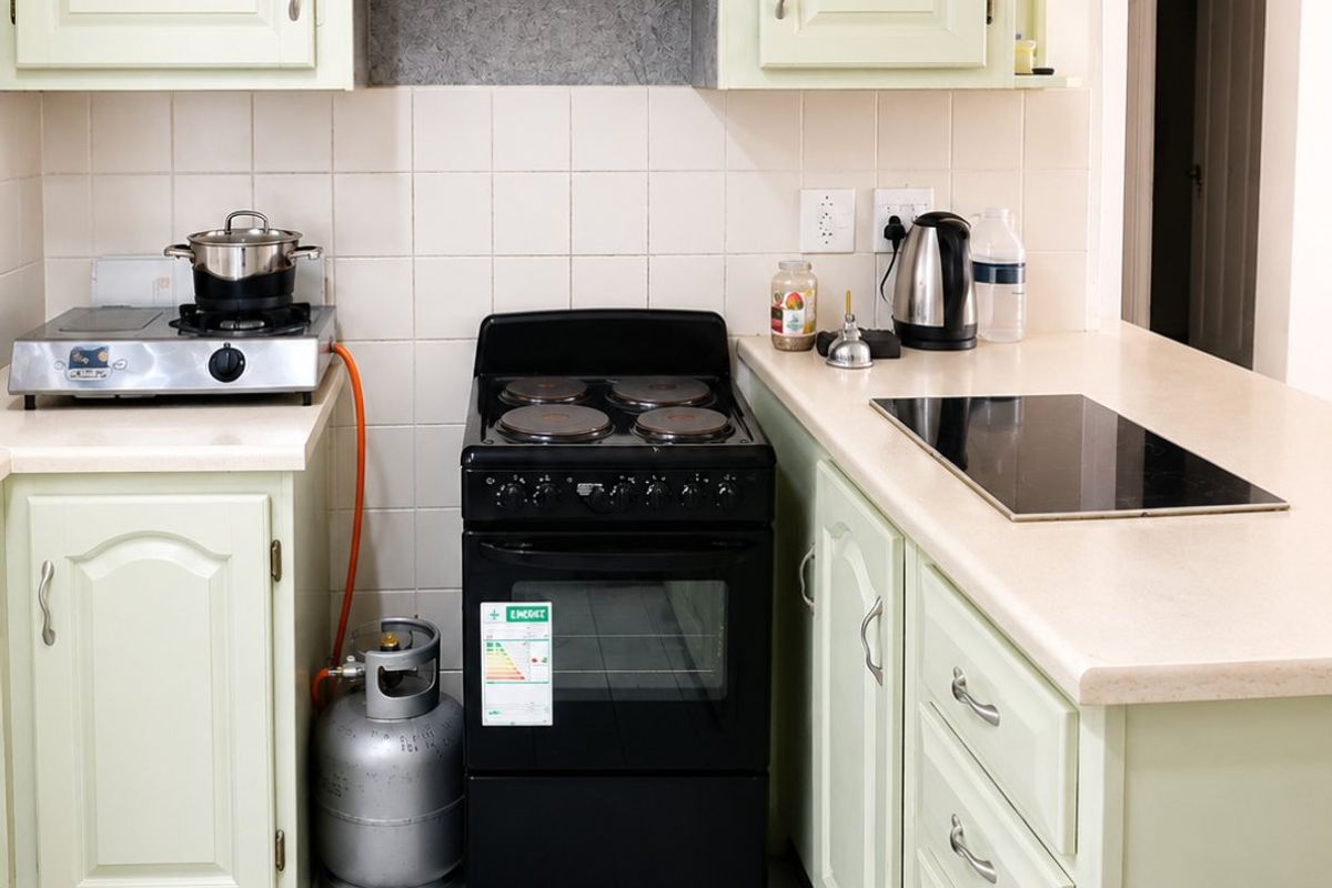 A functional kitchen featuring pale green cabinetry, laminate countertops, ceramic tile flooring, and a combination of electric stove and induction hob cooking surfaces.