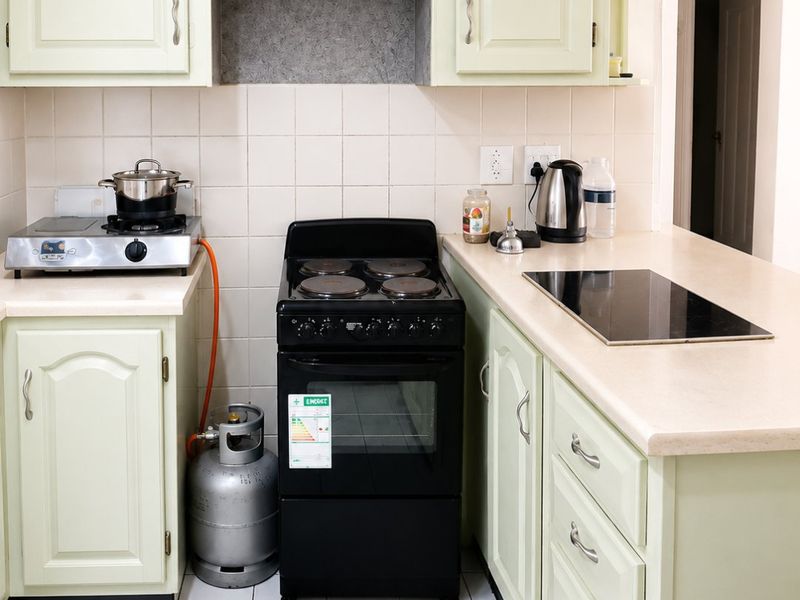 A functional kitchen featuring pale green cabinetry, laminate countertops, ceramic tile flooring, and a combination of electric stove and induction hob cooking surfaces.