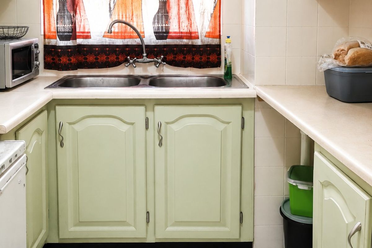 A functional kitchen featuring light green cabinetry, laminate countertops, a double sink with a mixer tap, and tiled flooring.