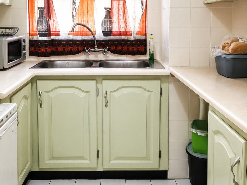 A functional kitchen featuring light green cabinetry, laminate countertops, a double sink with a mixer tap, and tiled flooring.