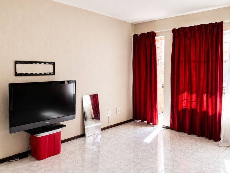 A bright, tiled living room featuring a wall-mounted television bracket and direct access to an outdoor area through a sliding door.