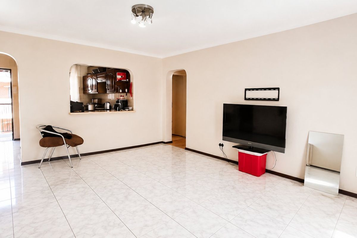 Spacious living area featuring neutral walls, tiled flooring, and a convenient pass-through window connecting to the kitchen area.