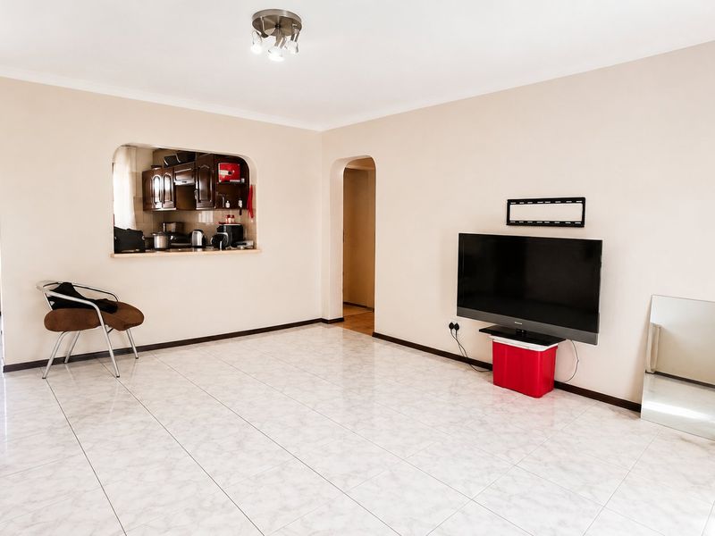 Spacious living area featuring neutral walls, tiled flooring, and a convenient pass-through window connecting to the kitchen area.