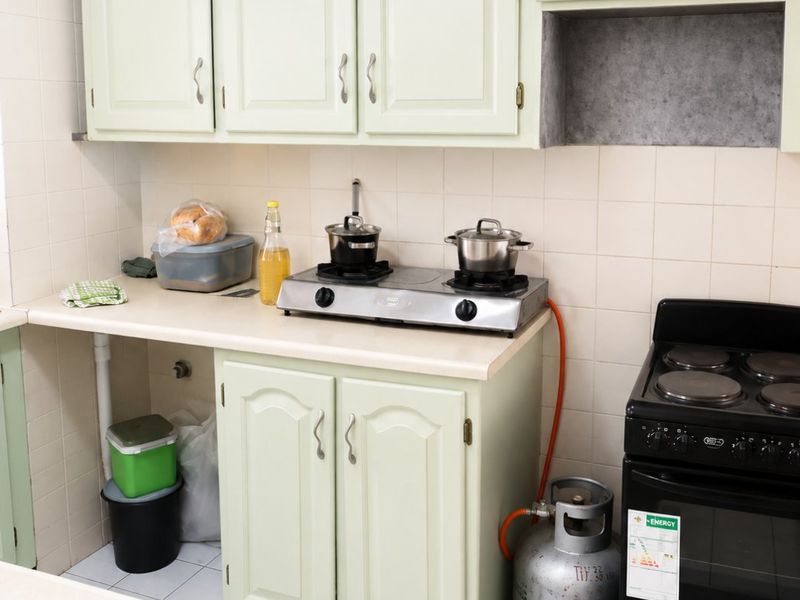 A functional kitchen featuring light green cabinetry, tiled backsplash, a gas cooktop, and a standalone electric oven with tiled flooring.