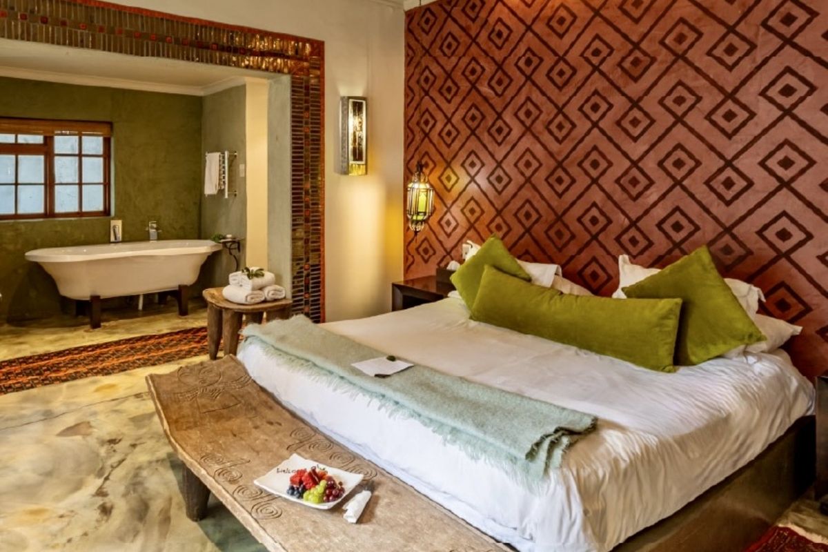 A well-appointed bedroom featuring a unique patterned feature wall, polished concrete floors, and an open-plan en-suite bathroom with a classic freestanding bathtub.
