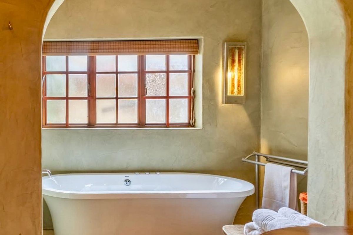 A serene bathroom featuring a freestanding bathtub set within an arched alcove, complemented by warm textured walls and a timber-framed window.