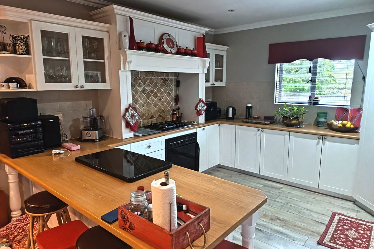 A well-maintained kitchen featuring white cabinetry, wooden countertops, a breakfast bar, and a built-in gas hob with a decorative tiled backsplash.