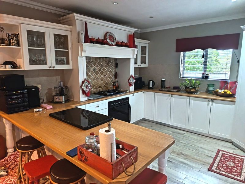 A well-maintained kitchen featuring white cabinetry, wooden countertops, a breakfast bar, and a built-in gas hob with a decorative tiled backsplash.