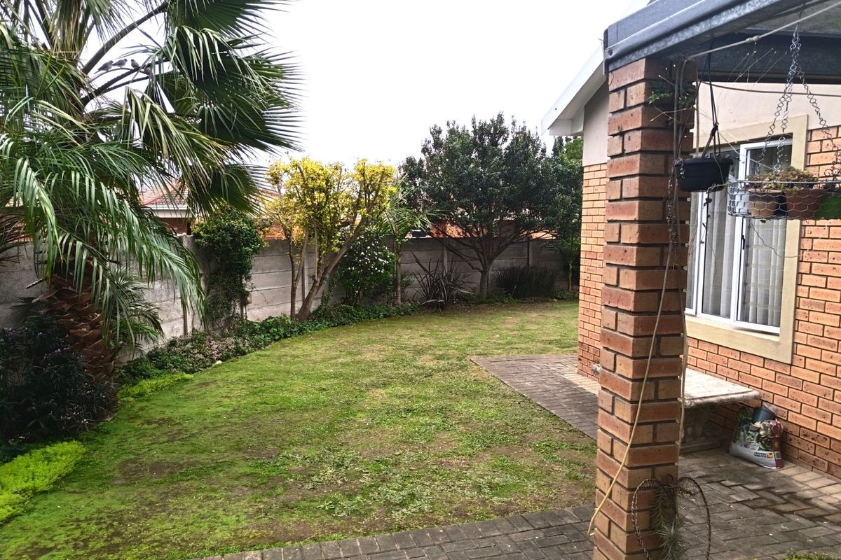 A rear garden view featuring a paved patio area, brick pillar support, and a lawn enclosed by a precast concrete boundary wall.
