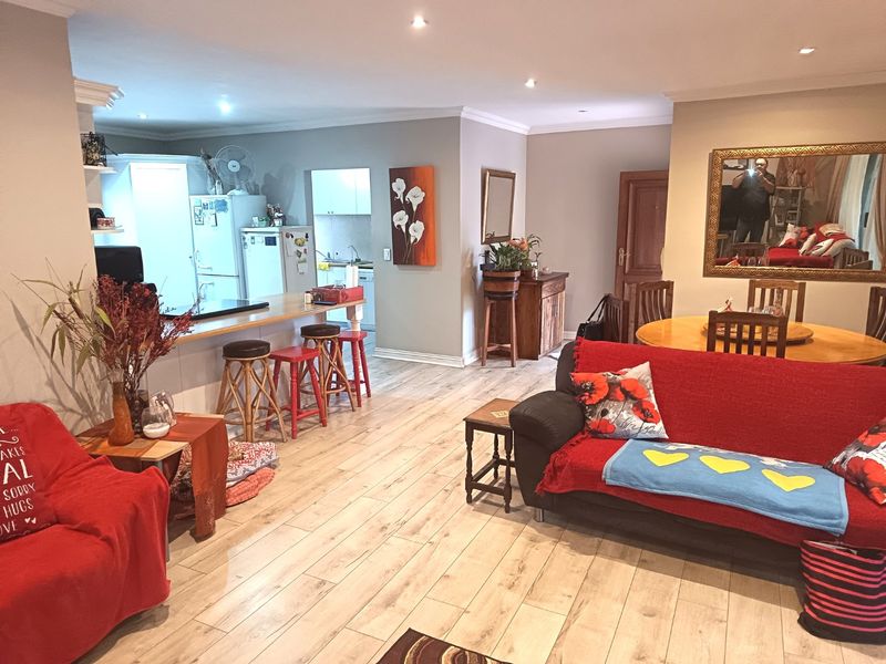 Open-plan living and dining area featuring light wood-look laminate flooring, recessed lighting, and a breakfast bar connecting to a functional kitchen and scullery space.