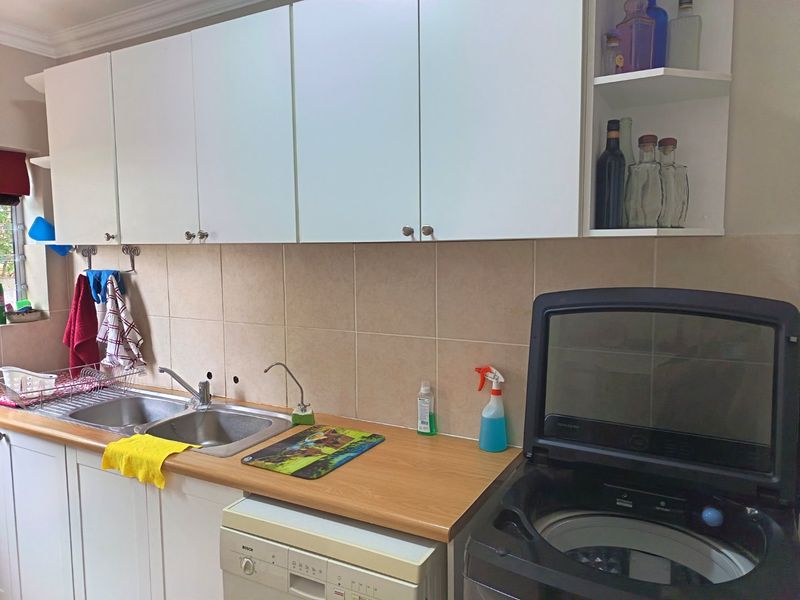 A functional laundry area featuring white built-in cabinetry, a stainless steel double sink, tiled backsplash, and laminate countertops.