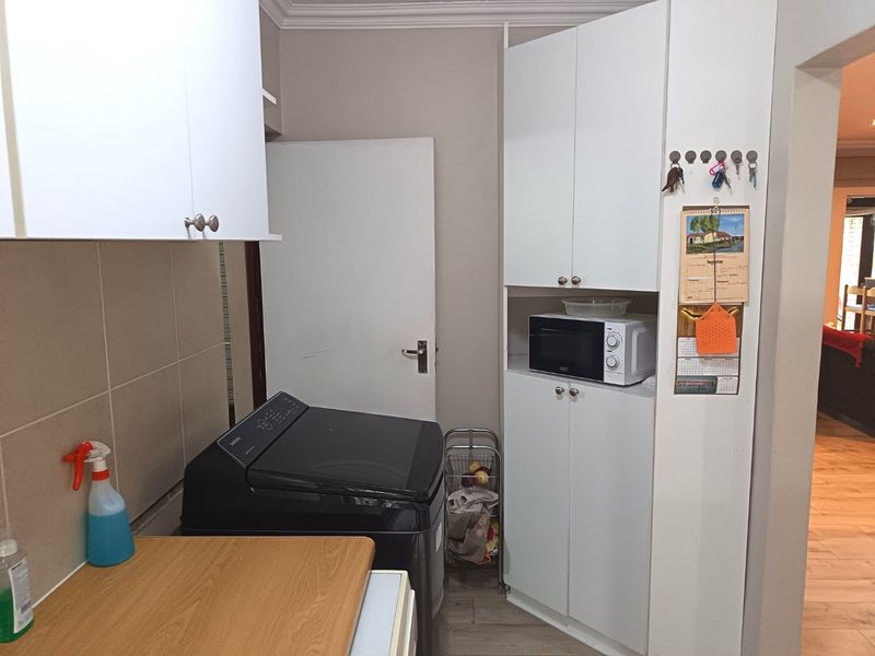 A functional laundry area featuring white built-in cabinetry, tiled splashback, and dedicated space for laundry appliances.