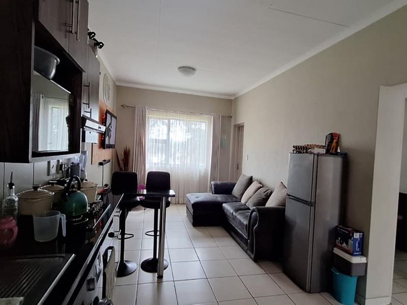 Open-plan living area featuring a compact kitchen with built-in cabinetry and a breakfast counter, flowing into a comfortable lounge space with tiled flooring.