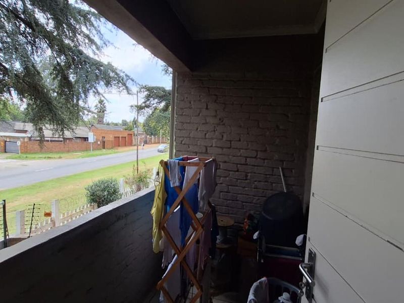 A covered balcony area featuring exposed brickwork and a concrete balustrade, offering an outdoor space with views of the surrounding street and neighborhood.