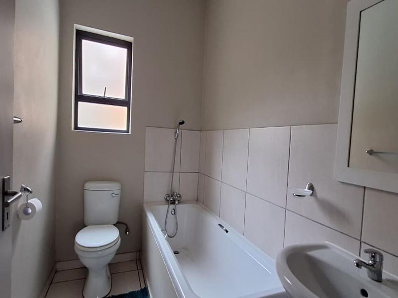 A functional bathroom featuring a bathtub with shower mixer, pedestal sink, and toilet, finished with neutral wall tiles.
