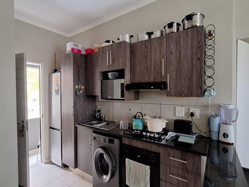 Compact kitchen featuring dark wood-grain cabinetry, granite countertops, built-in oven, gas hob, and integrated laundry plumbing, offering a functional and modern workspace.