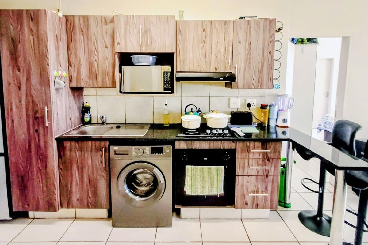 Compact kitchen featuring wood-look laminate cabinetry, granite countertops, built-in oven with gas hob, and integrated laundry appliance space.