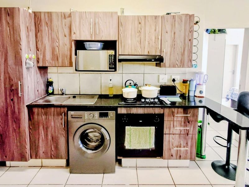 Compact kitchen featuring wood-look laminate cabinetry, granite countertops, built-in oven with gas hob, and integrated laundry appliance space.