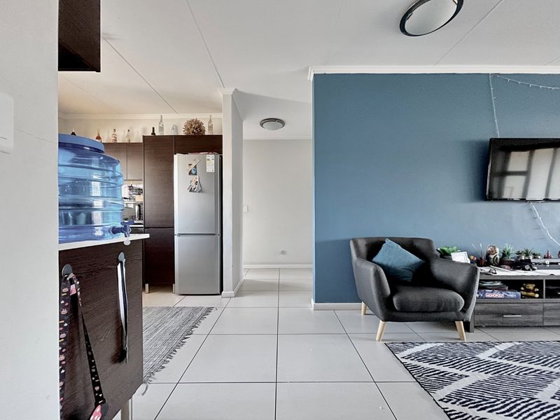 Open plan living area featuring tiled flooring and a transition into the kitchen space with dark cabinetry.