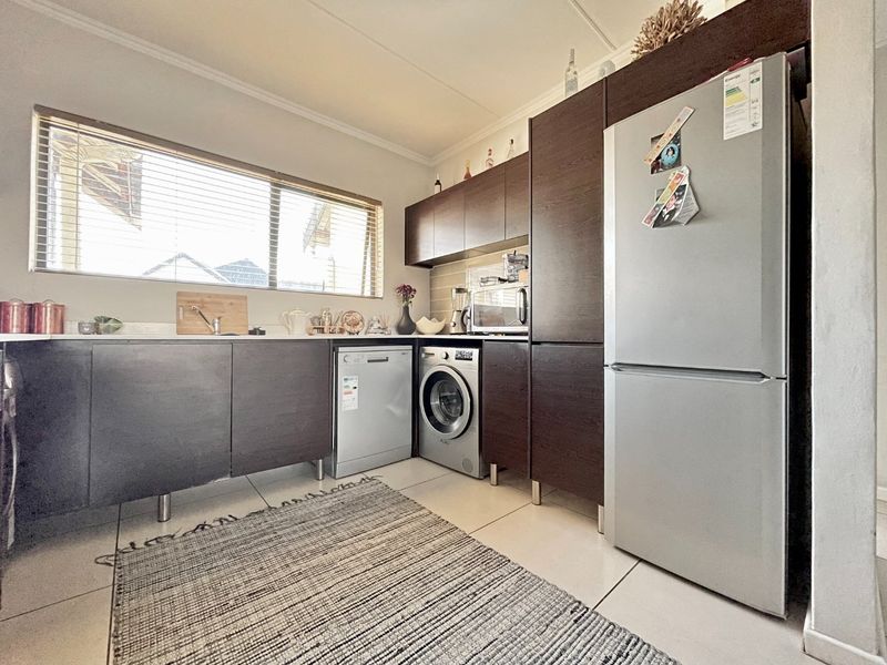 A functional kitchen featuring dark wood cabinetry, tiled flooring, a built-in sink, and a tiled backsplash with integrated appliance spaces.