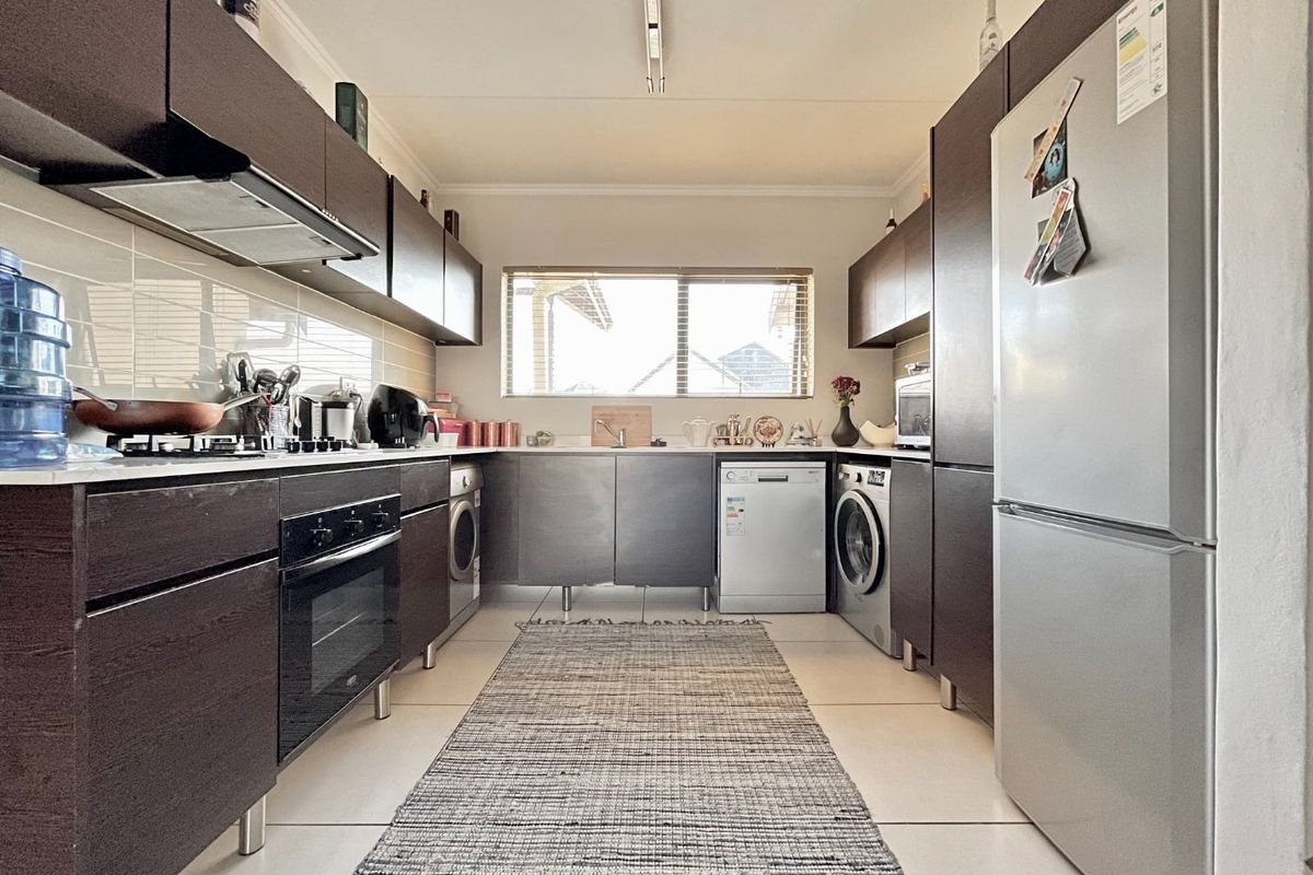 A functional galley-style kitchen featuring dark wood cabinetry, integrated appliances, tiled splashbacks, and light-colored floor tiles.