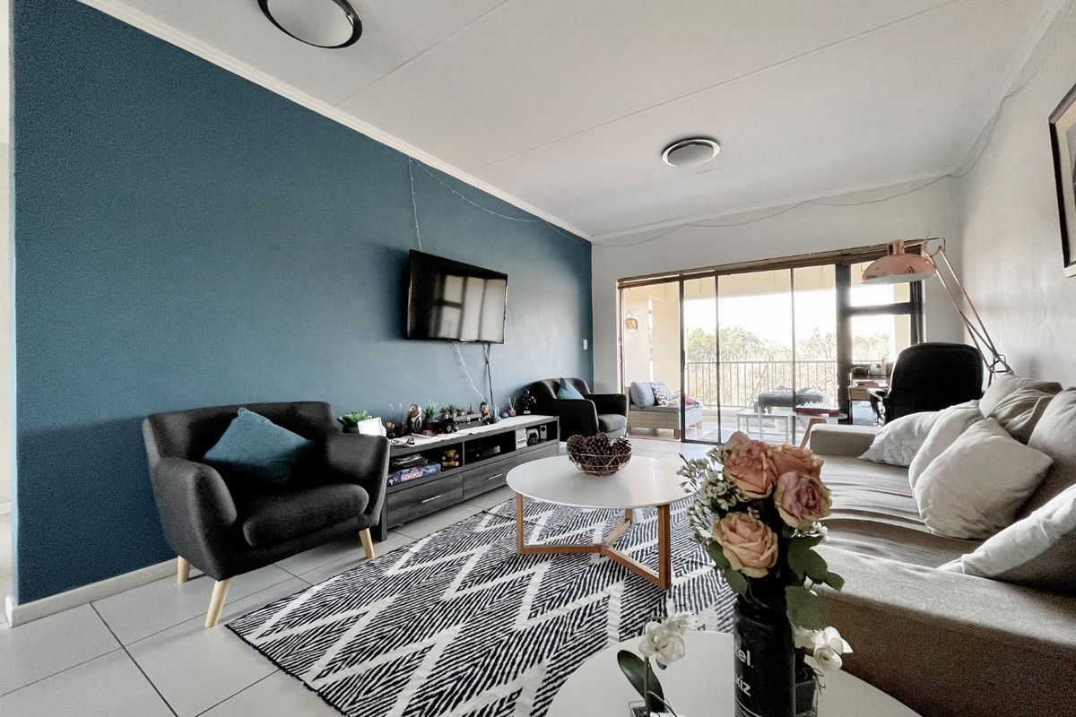 A well-lit living room featuring tiled flooring, a bold accent wall, and large sliding glass doors that provide access to an outdoor balcony area.