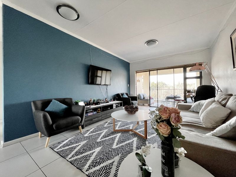 A well-lit living room featuring tiled flooring, a bold accent wall, and large sliding glass doors that provide access to an outdoor balcony area.