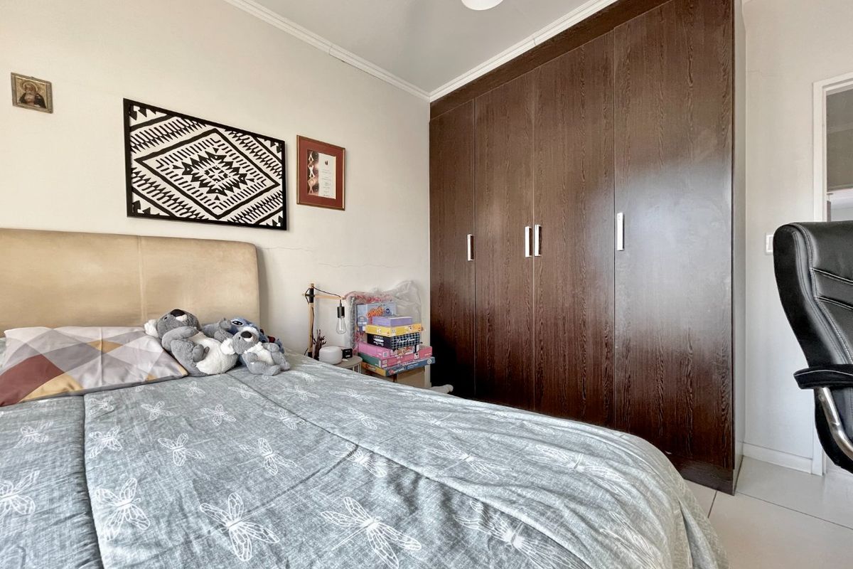 A bedroom featuring a large dark wood built-in wardrobe, tiled flooring, and neutral wall finishes.