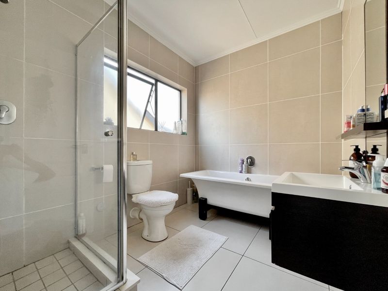 Modern bathroom featuring a freestanding bathtub, glass-enclosed shower, wall-mounted toilet, and a sleek vanity cabinet with neutral floor-to-ceiling tiling.