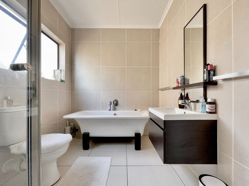Modern bathroom featuring a freestanding bathtub, wall-mounted vanity, neutral wall and floor tiling, and a separate shower enclosure.