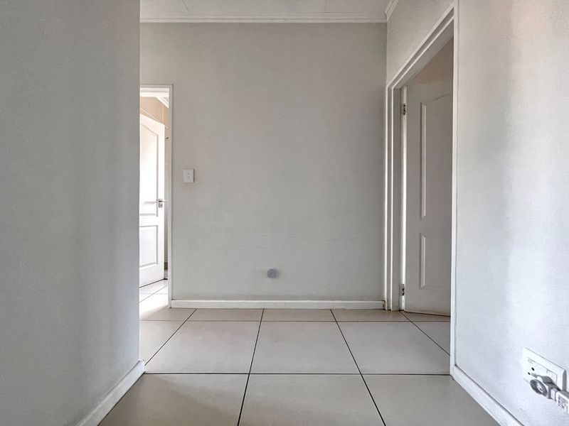 A clean, empty hallway featuring neutral tiled flooring and access to multiple rooms through standard internal doors.
