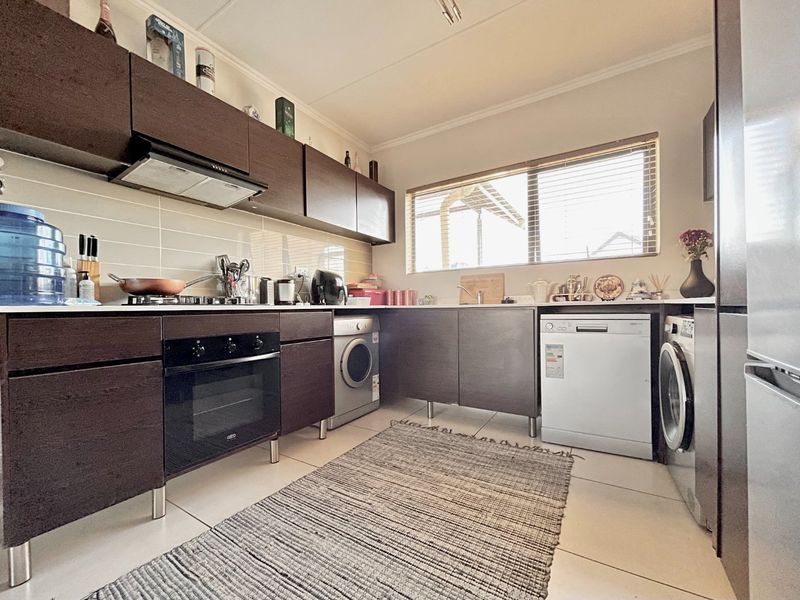 Functional kitchen featuring dark wood cabinetry, built-in oven, gas hob, extractor fan, and integrated laundry appliance connections with tiled flooring.