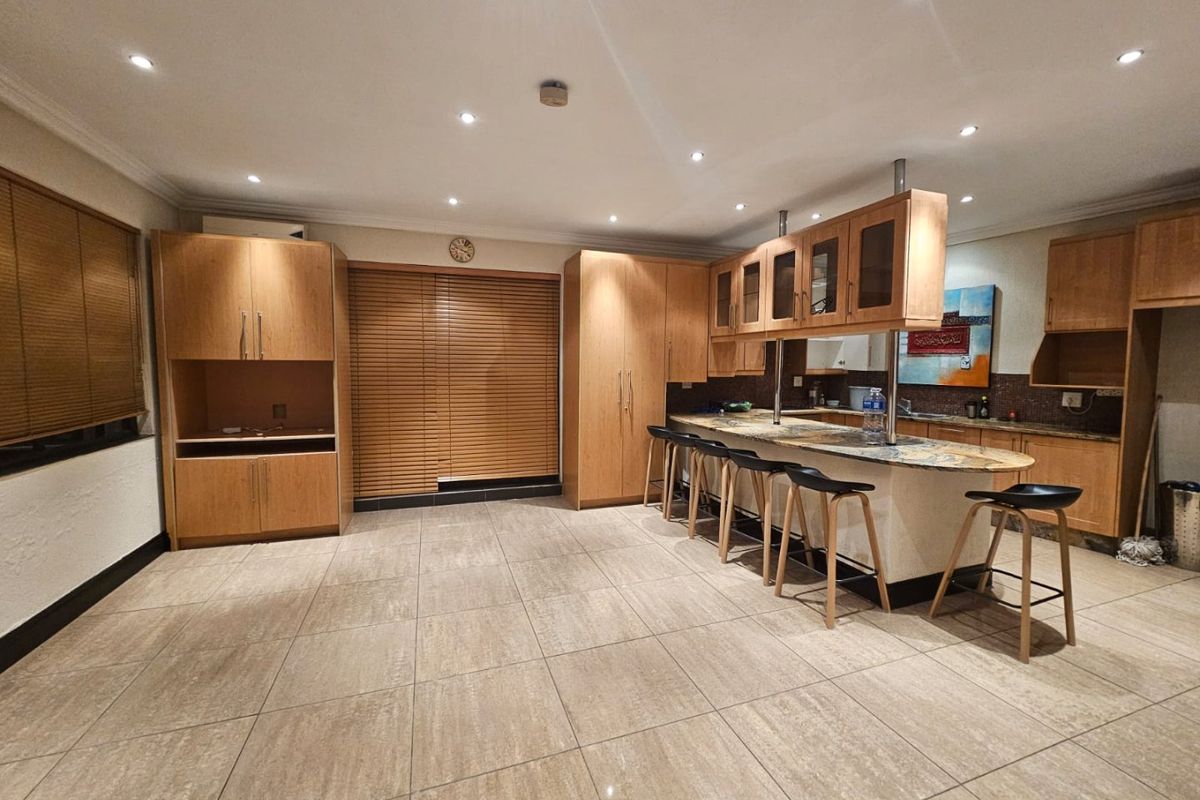 Spacious open-plan kitchen featuring extensive wooden cabinetry, stone countertops, a breakfast bar, and neutral tiled flooring with recessed lighting throughout.