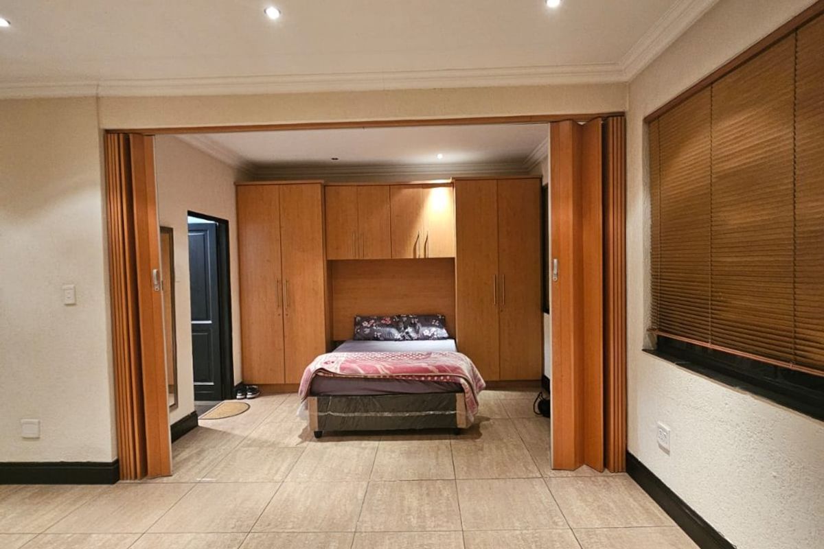 Bedroom featuring built-in wooden cupboards, tiled flooring, recessed lighting, and folding doors that open into the main living area.