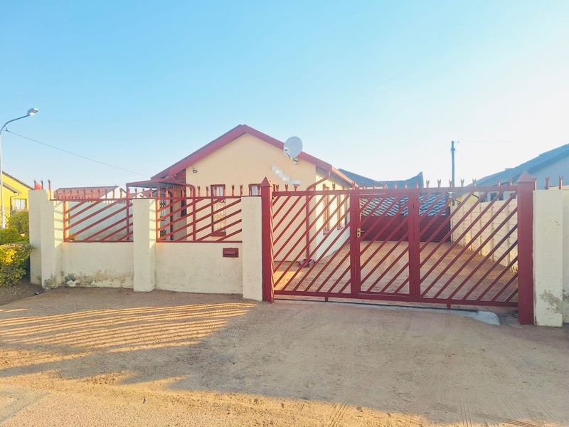 Front exterior view of a house featuring a gated driveway, perimeter wall with security fencing, and a tiled roof.