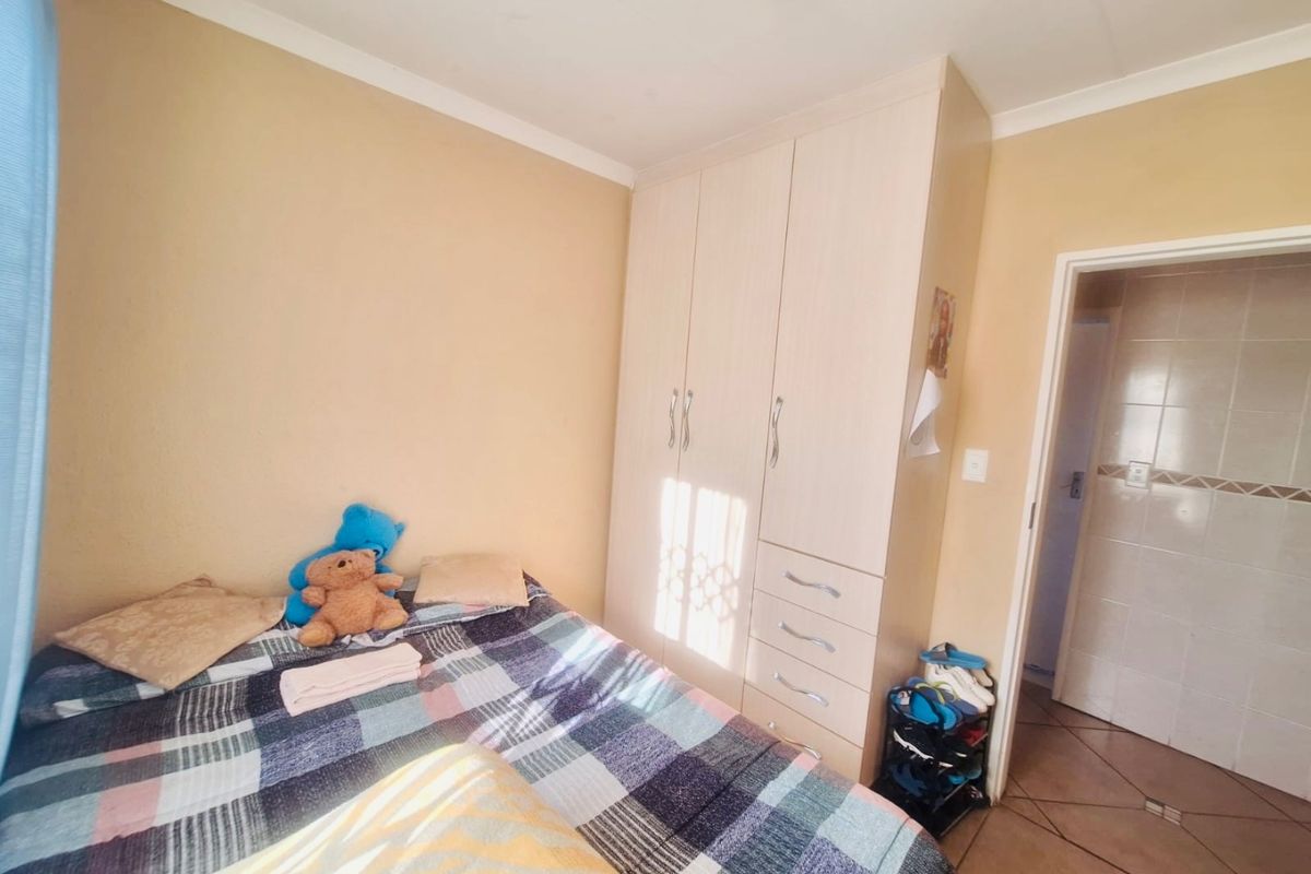 A bedroom featuring built-in wardrobes and tiled flooring, with an adjacent doorway leading to a tiled bathroom area.