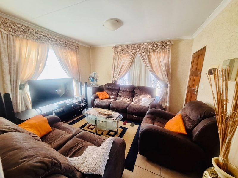 A comfortable living room featuring tiled flooring, neutral wall finishes, and natural light through large windows with traditional curtain treatments.