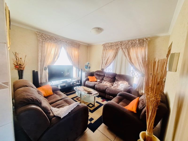 A comfortable living room featuring tiled flooring and large windows with curtain rails, providing a functional and well-lit space for relaxation.